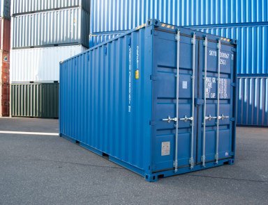 Blue 20ft high cube shipping container, rear three-quarter view with closed doors and locking bars in a container yard